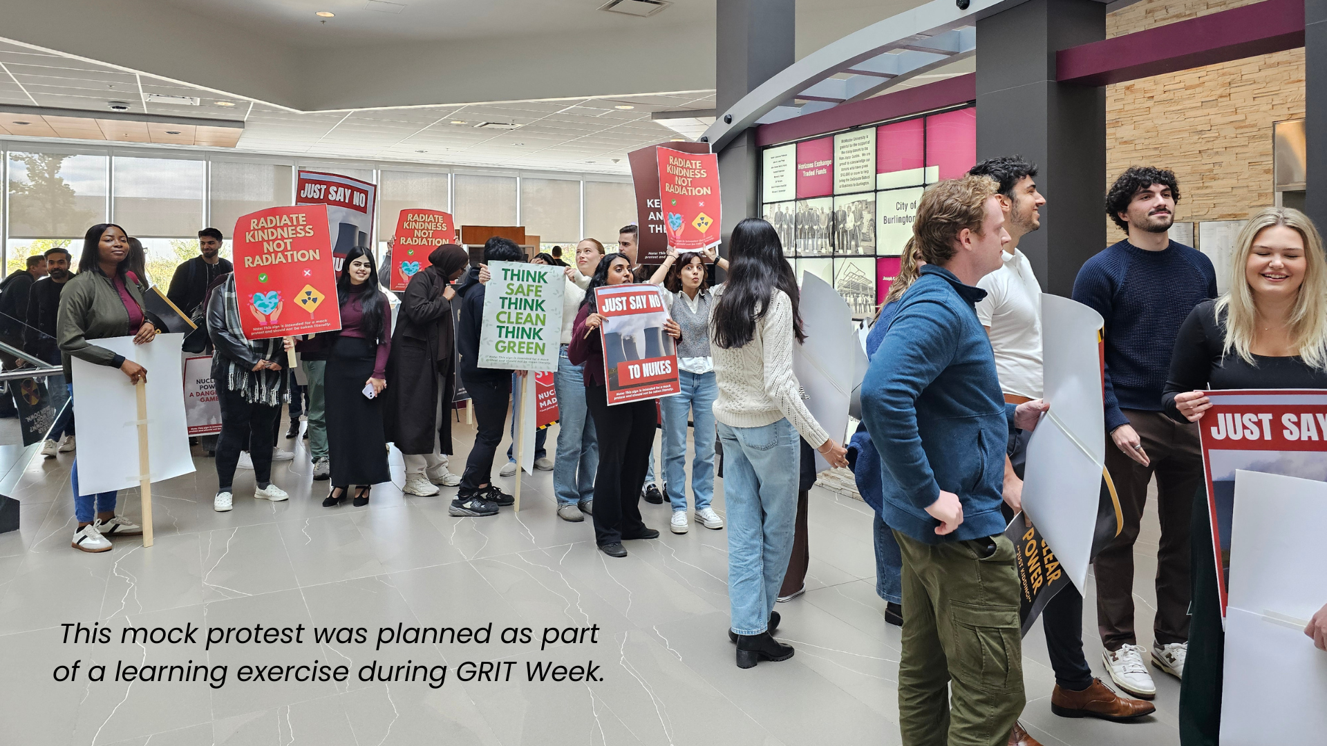 A group of mock protestors in a lobby holding signs against nuclear energy, disrupting a DeGroote MBA lecture.