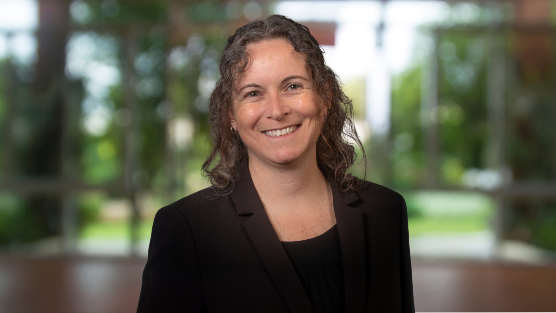 Trish Ruebottom, a woman in a black suit and shirt, smiles confidently, exuding professionalism and warmth.