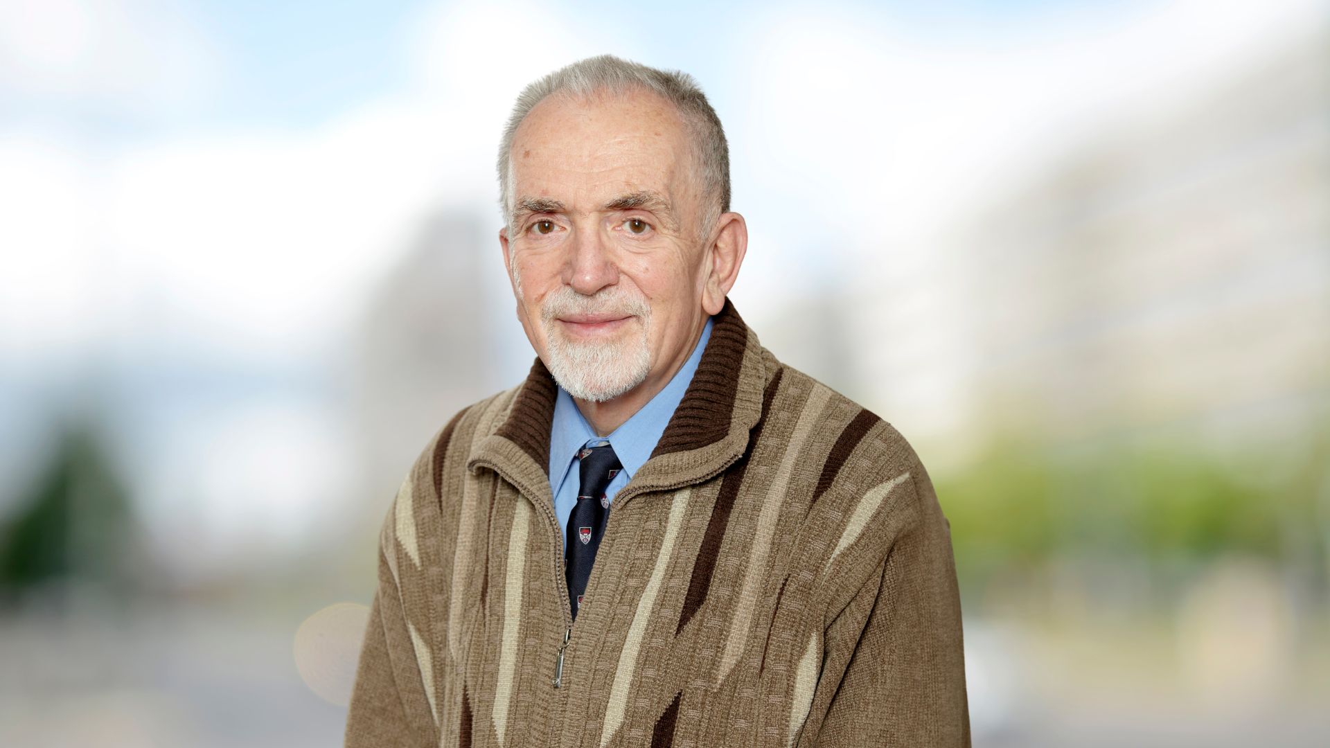 George Wesolowsky, an older man in a sweater and tie, smiles warmly.