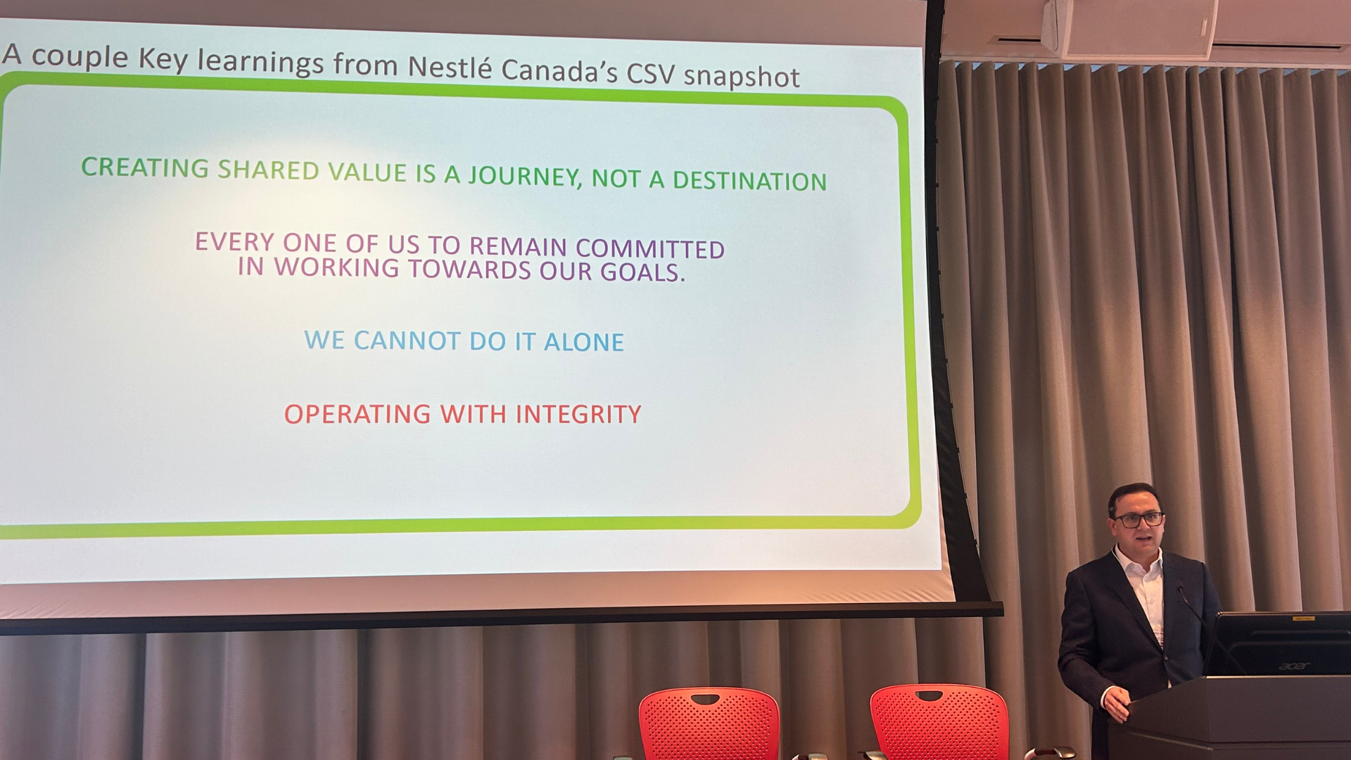 Matt Judd, presents from a podium, facing an audience with a presentation on Nestlé Canada.