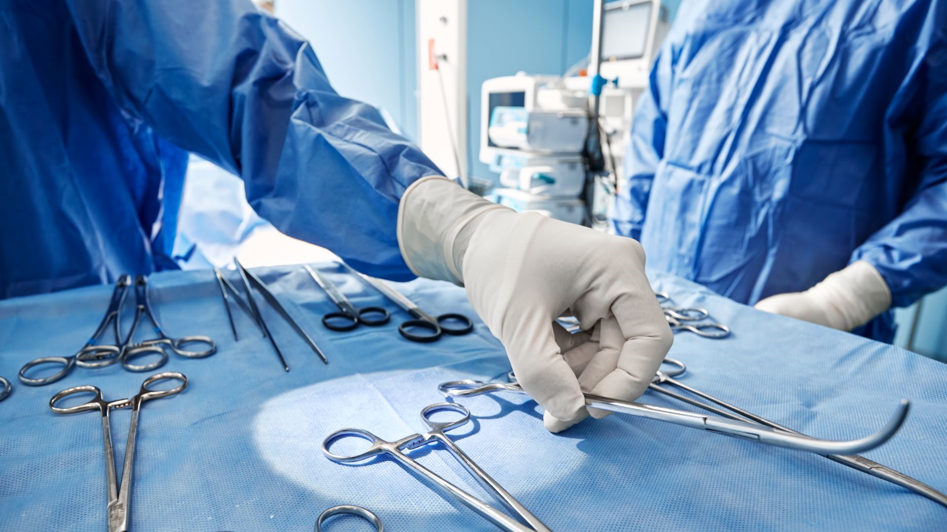 Gloved hand selecting surgical instrument from a sterile table in an operating room.