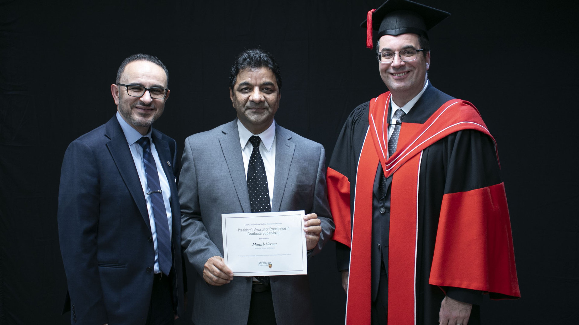 Three men in business attire showcase a certificate, highlighting Manish Verma's achievement in graduate supervision excellence.