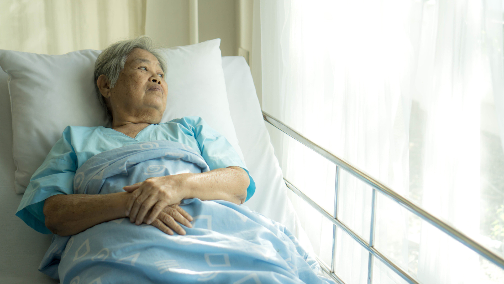 An elderly woman resting in a hospital bed, surrounded by medical equipment and soft lighting, conveying a sense of care.