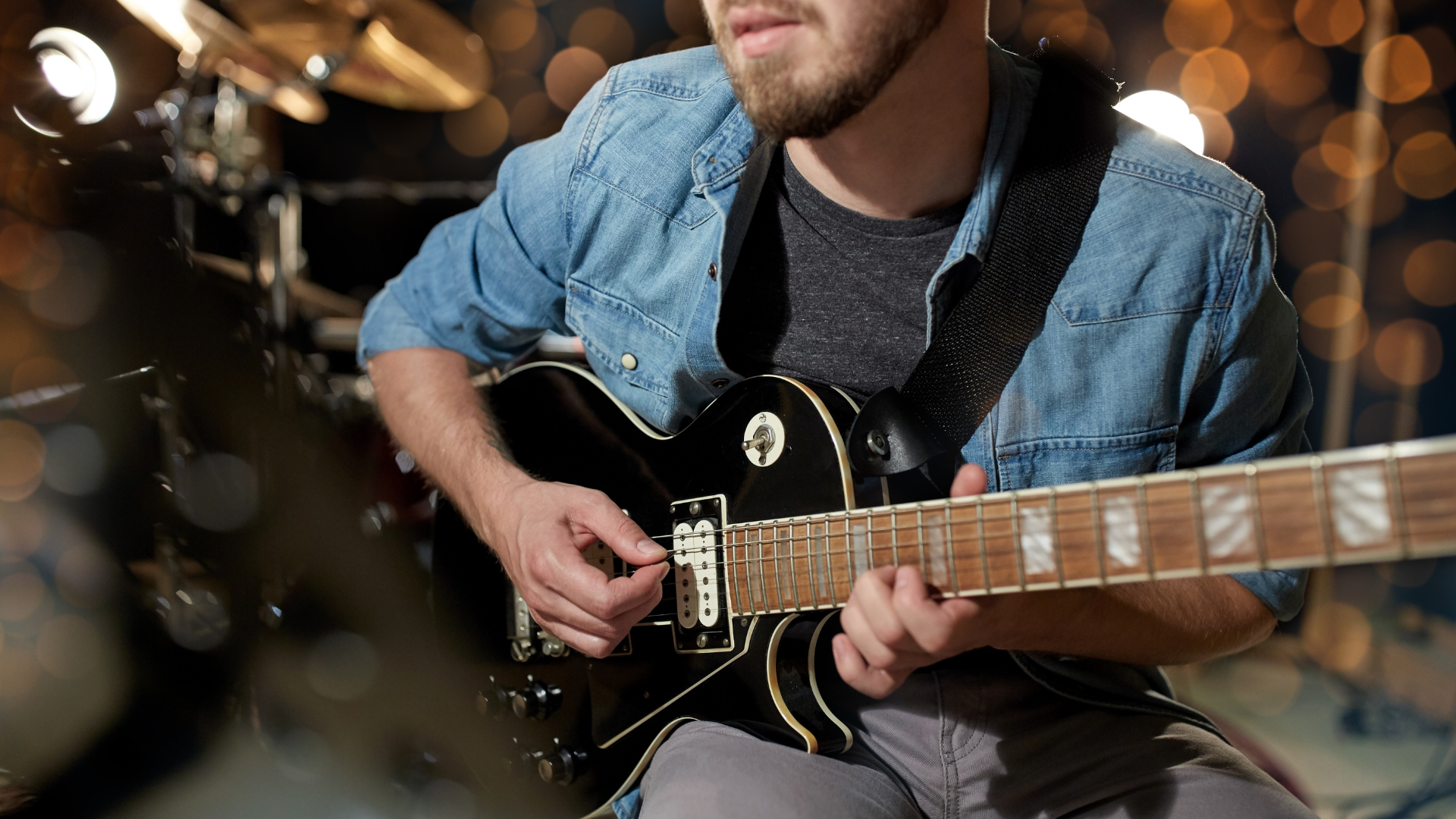 A man passionately plays an electric guitar, positioned in front of a vibrant drum kit, creating a dynamic musical scene.