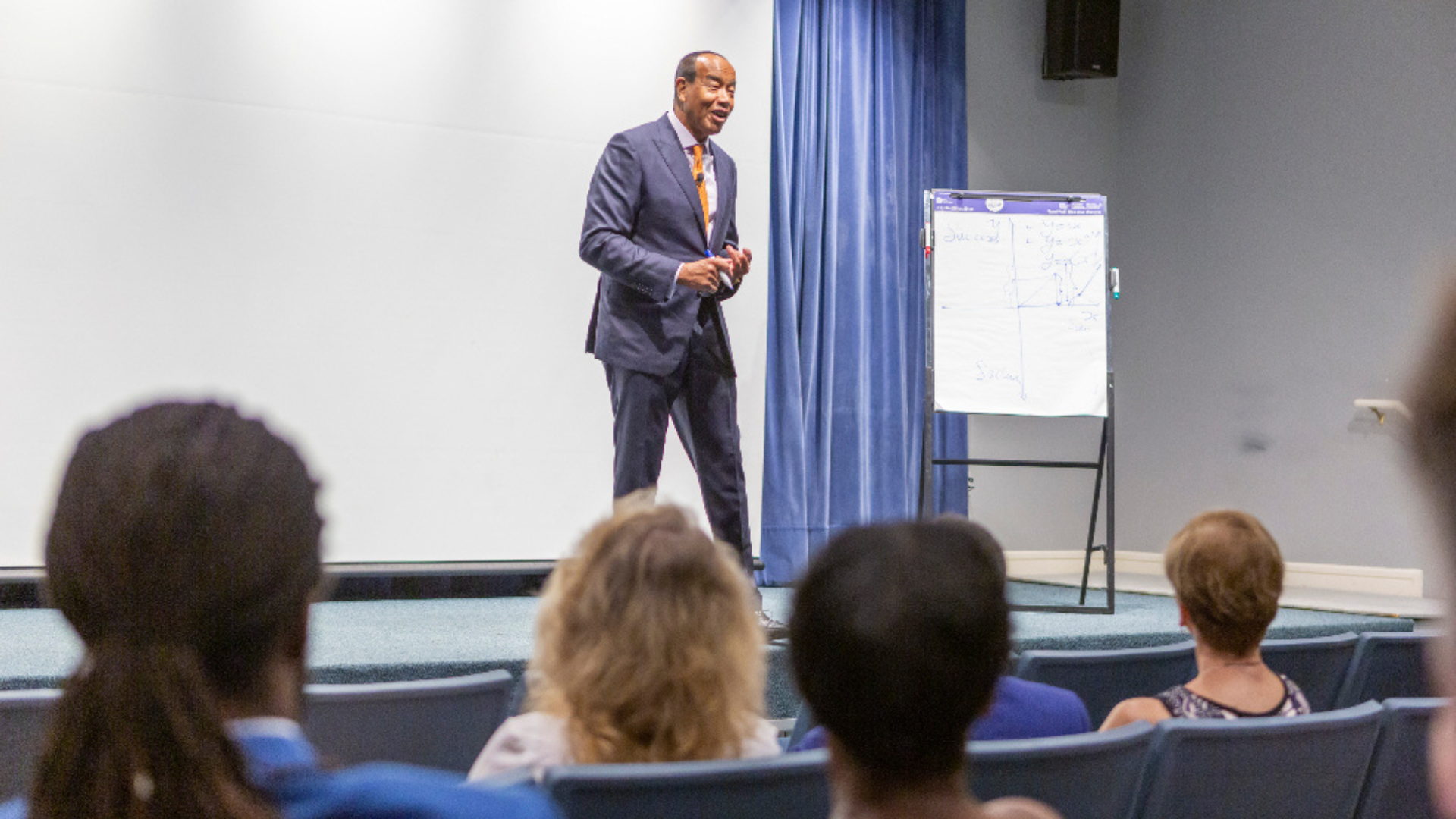 Michael Lee-Chin in a suit and tie delivers a presentation to an engaged audience, showcasing his expertise and insights.