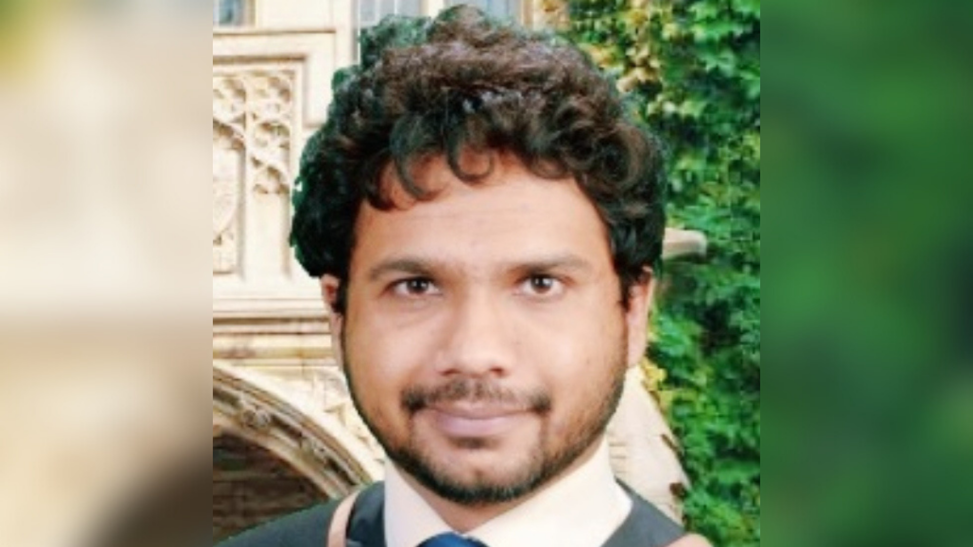 Mohit Verma, dressed in a suit and tie, smiles while standing in front of a contemporary building.