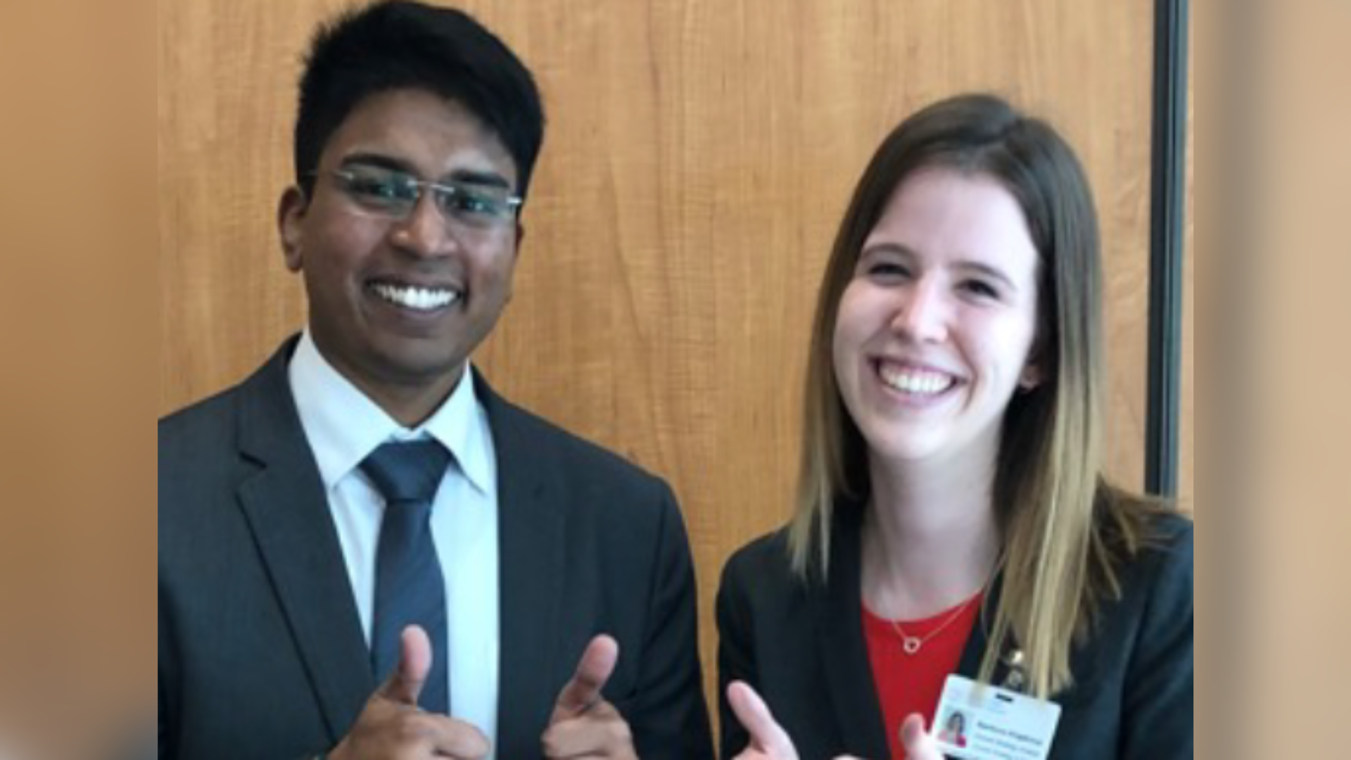 Two DeGroote MBA students in business attire smiling and giving a thumbs up