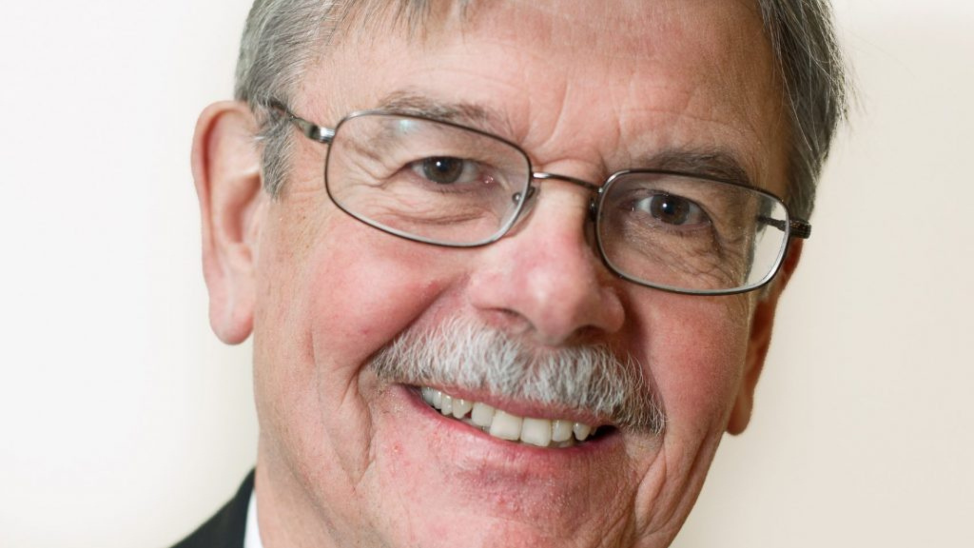 A close-up of Gordon Pitts, a man with glasses and a mustache, smiling warmly at the camera.