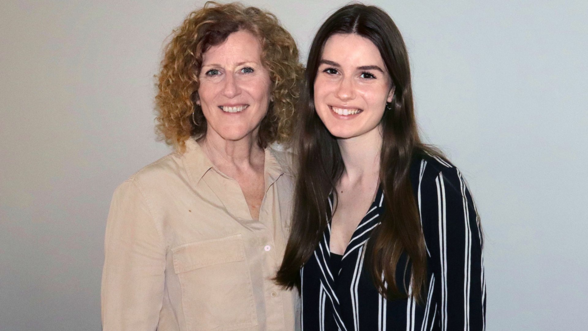 Rachel West and her mother stand side by side, smiling warmly in front of a plain white wall.