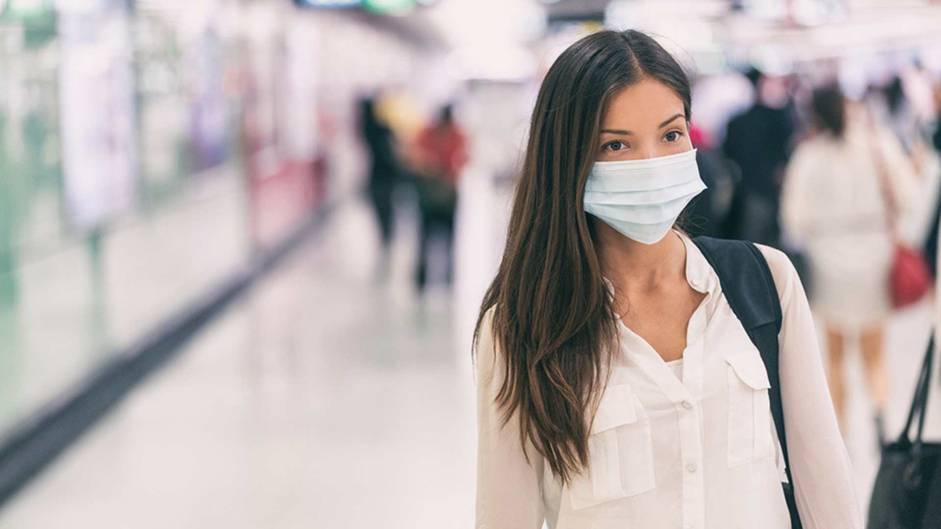 A woman wearing a face mask stands in an airport, highlighting health precautions during travel.