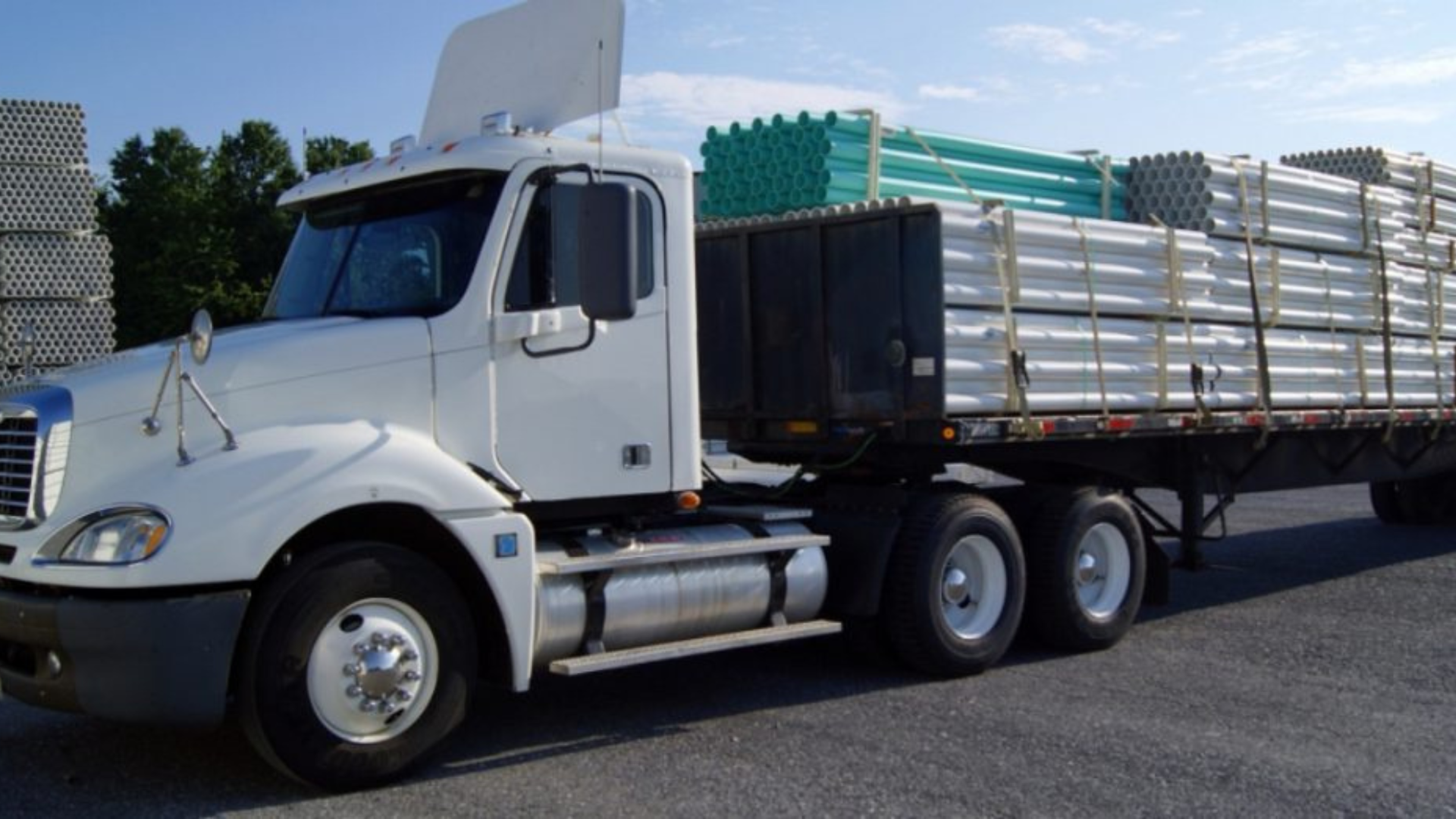 A white truck with a metal pipe-filled trailer, illustrating the vital role of transportation in the supply chain.