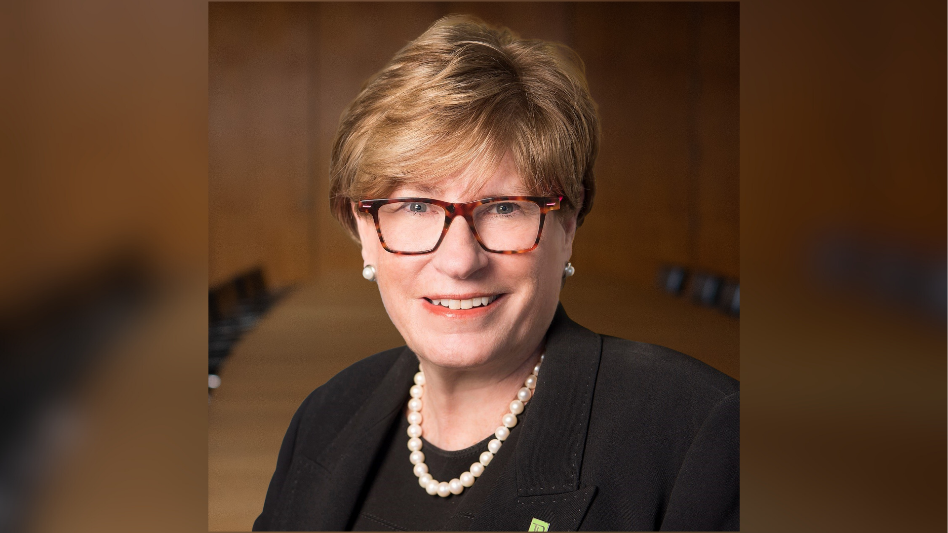 Karen Maidment, wearing glasses and a necklace, smiles while seated in a conference room.