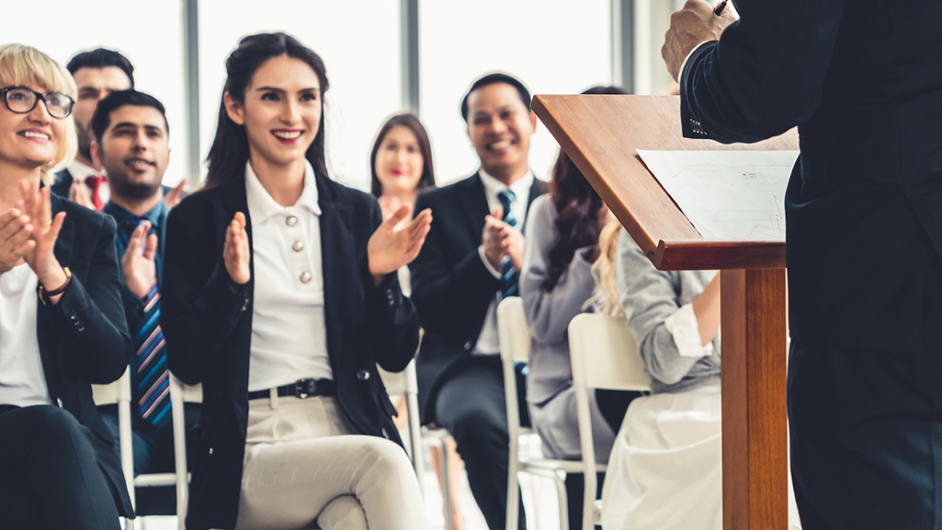 An engaged audience of business individuals applauding a presenter.