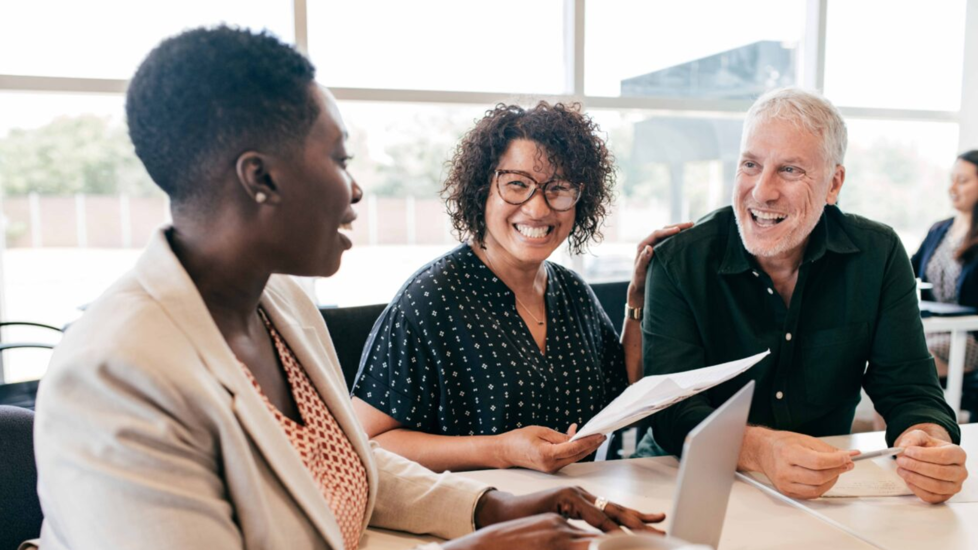 Three diverse individuals seated at a table, one person smiling, representing collaboration and diversity in education initiatives.