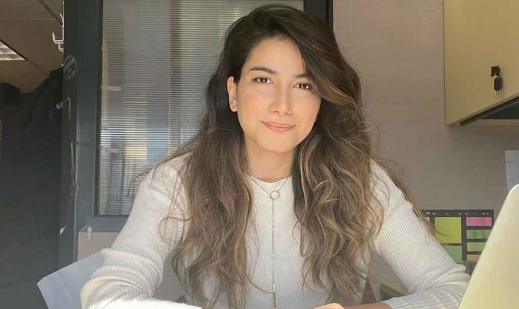 Farnaz Ghaedipour smiles while seated at her desk, engaged with her laptop.