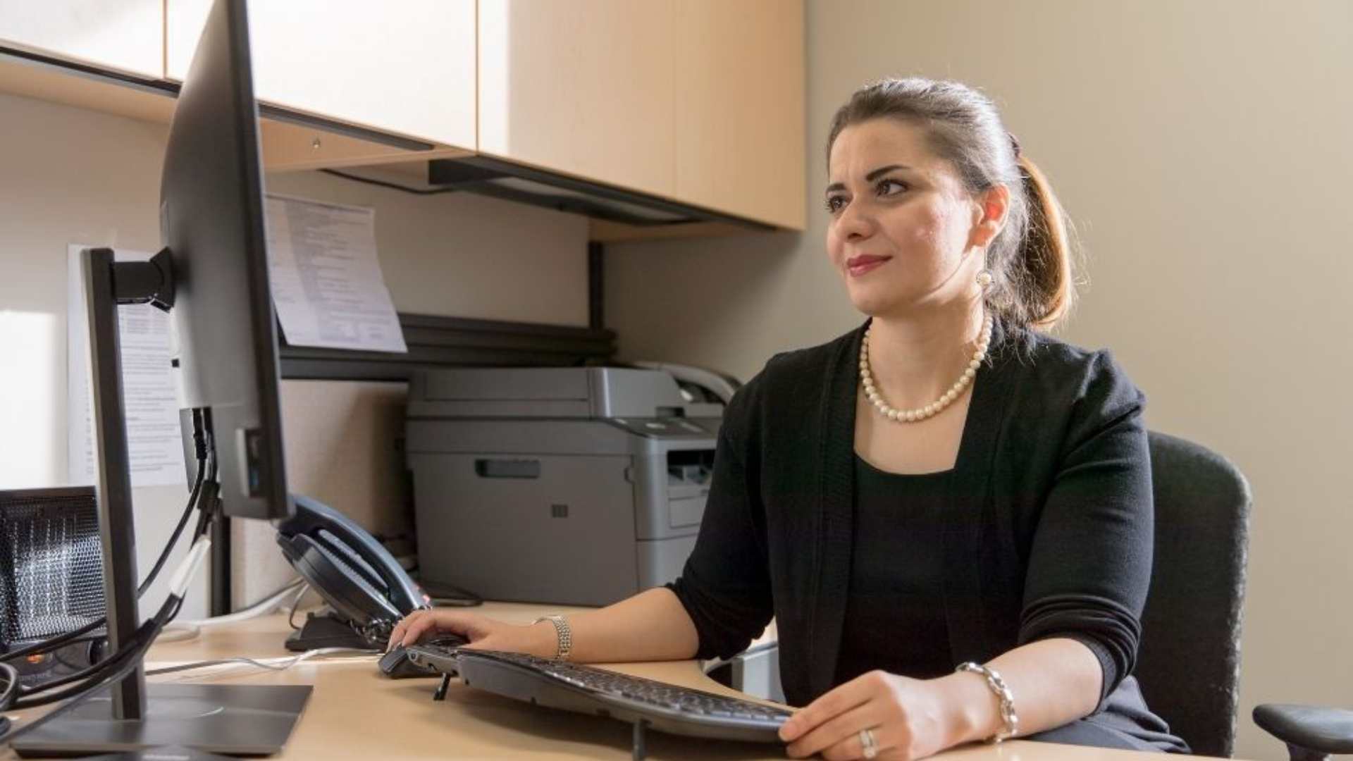 A professional woman seated at her desk, focused on her computer monitor.