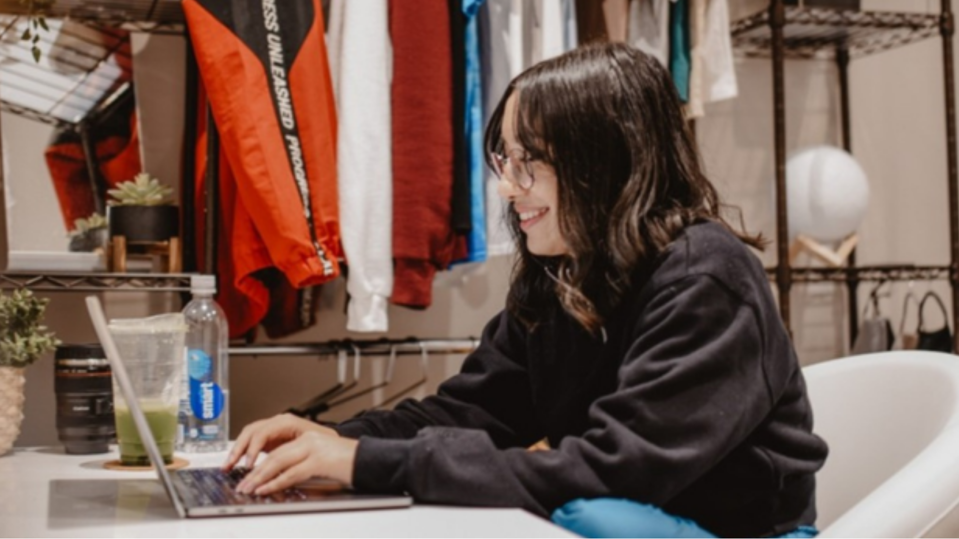 A woman seated at a desk, focused on typing on her laptop, surrounded by a tidy workspace.