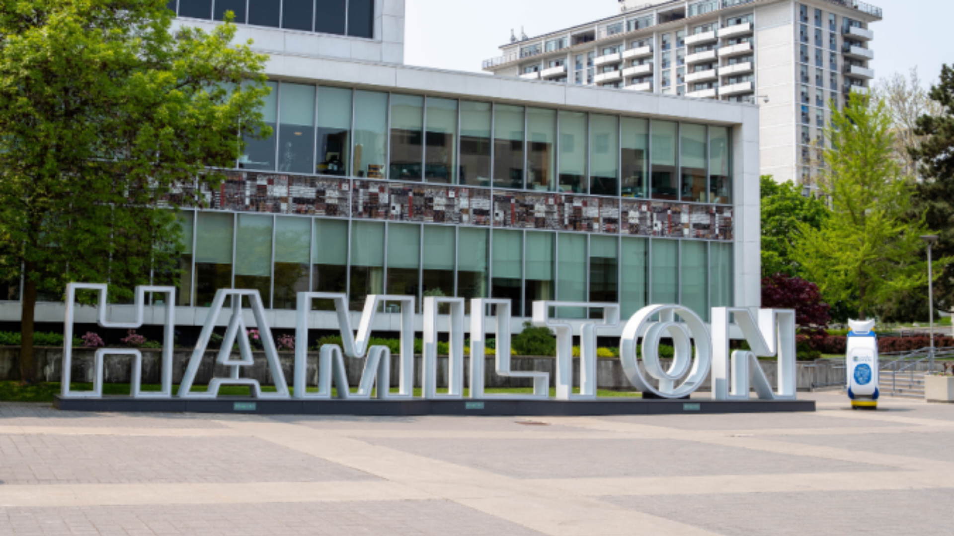 Large white letters spelling 'Hamilton' prominently displayed in front of Hamilton City Hall building.