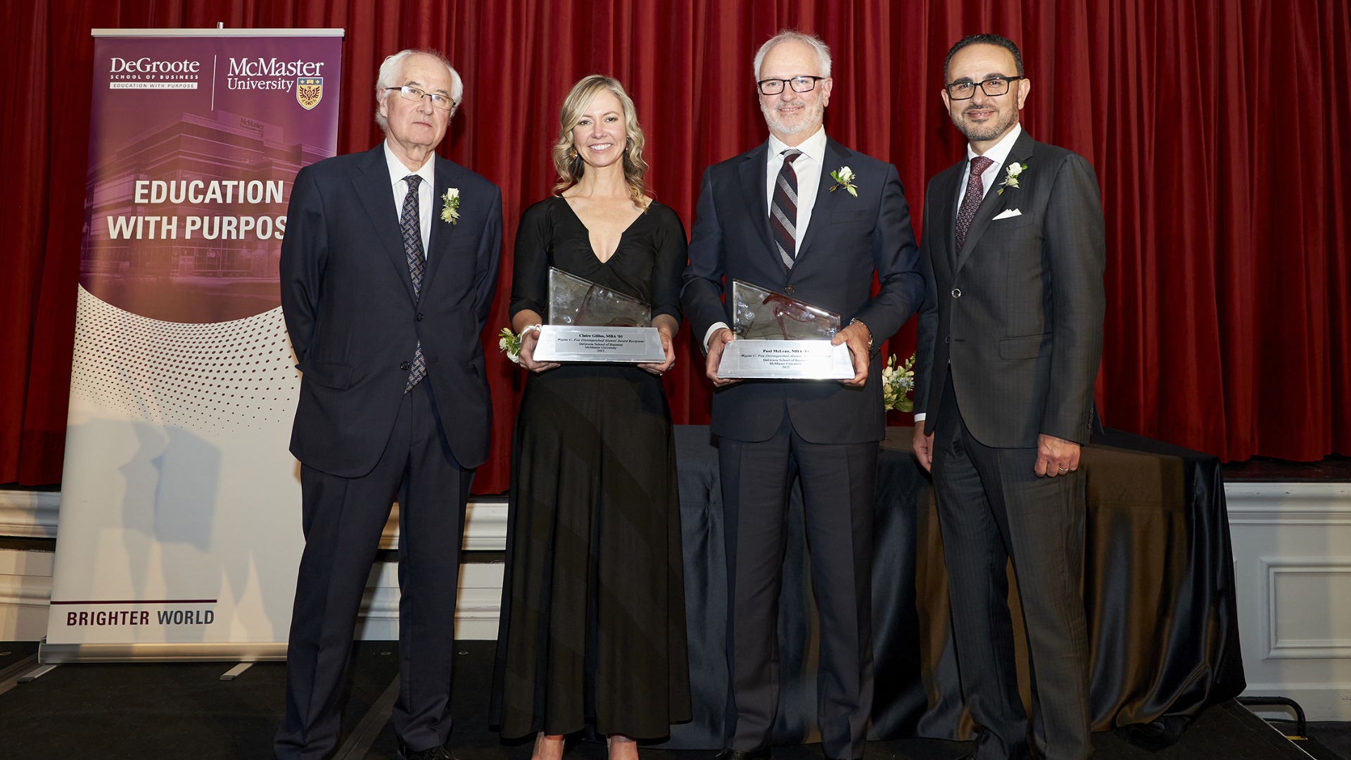 Four individuals, Wayne C. Fox, Claire Gillies, Paul McLean, and Dean Khaled Hassanein, stand before a red curtain with awards.