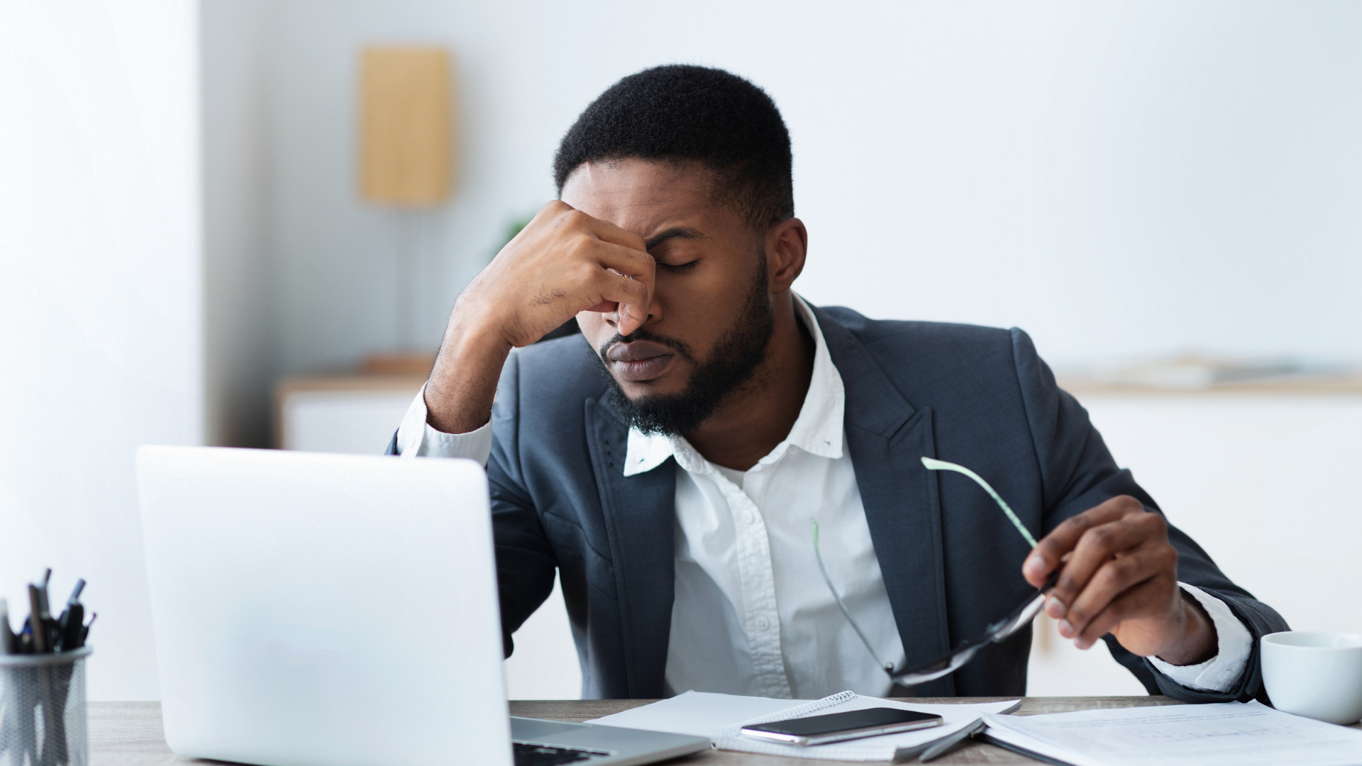 A man in a suit sits at a desk, head in hands, symbolizing the mental health crisis affecting Canadians today.