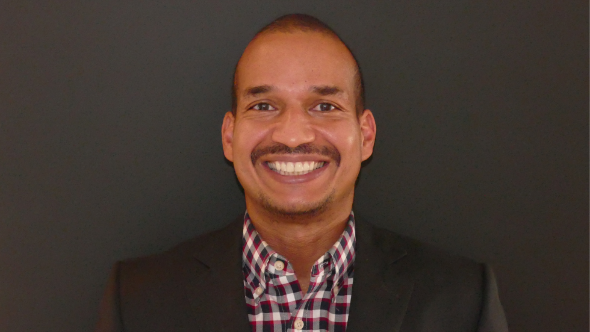 A smiling Earl Davis poses for the camera in a black jacket, complemented by a checkered shirt.