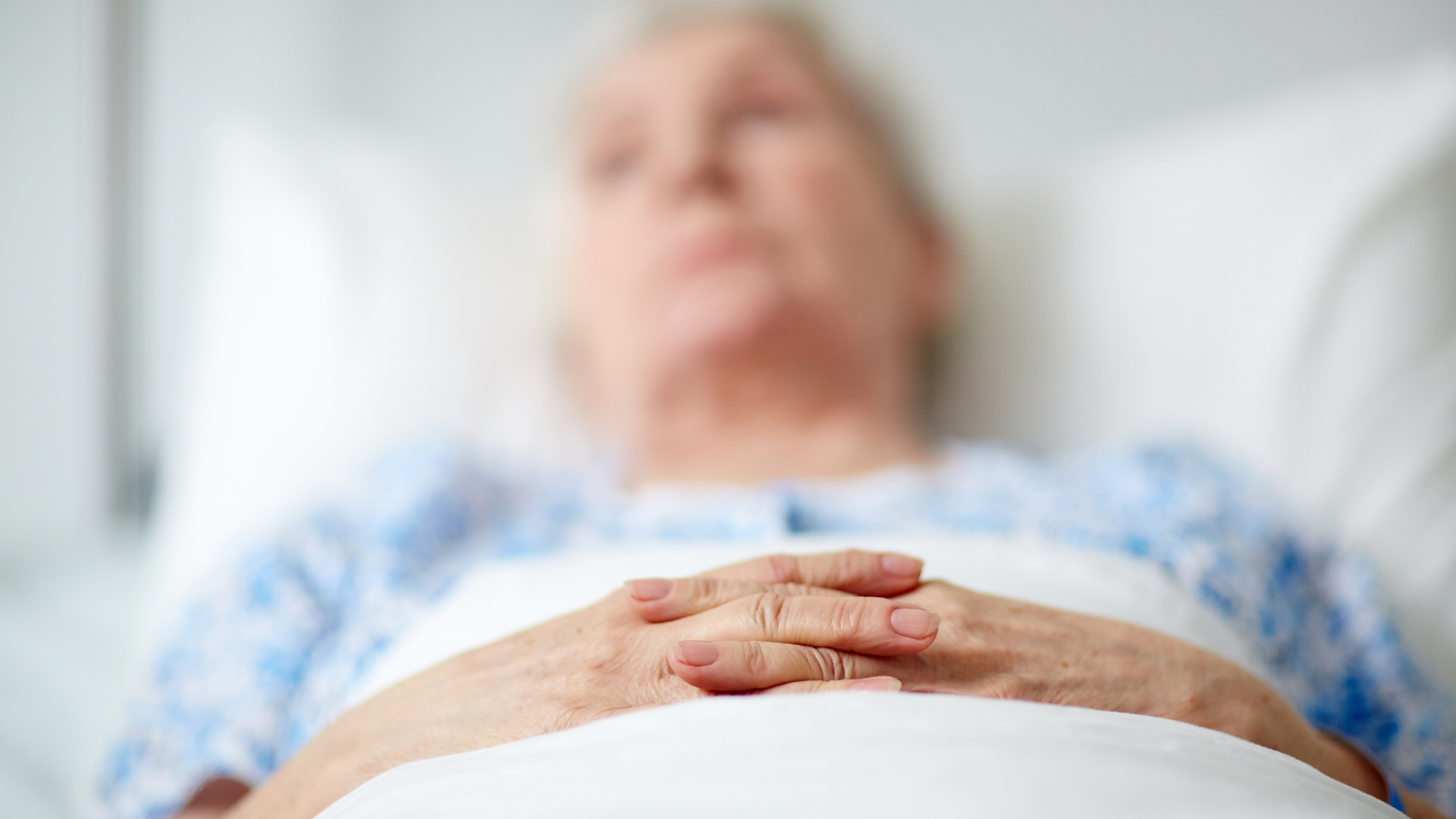 An elderly woman in bed with her hands on her chest, illustrating concerns over care quality amid new 'More Beds' legislation.