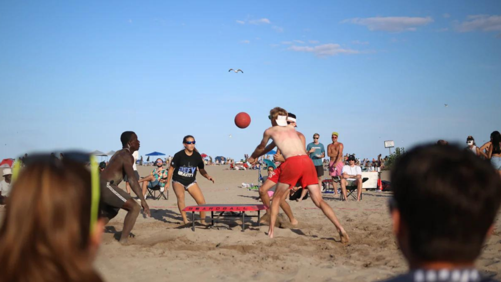 A group of young people playing boardball on the beach, enjoying the sun and sand in a lively outdoor setting.