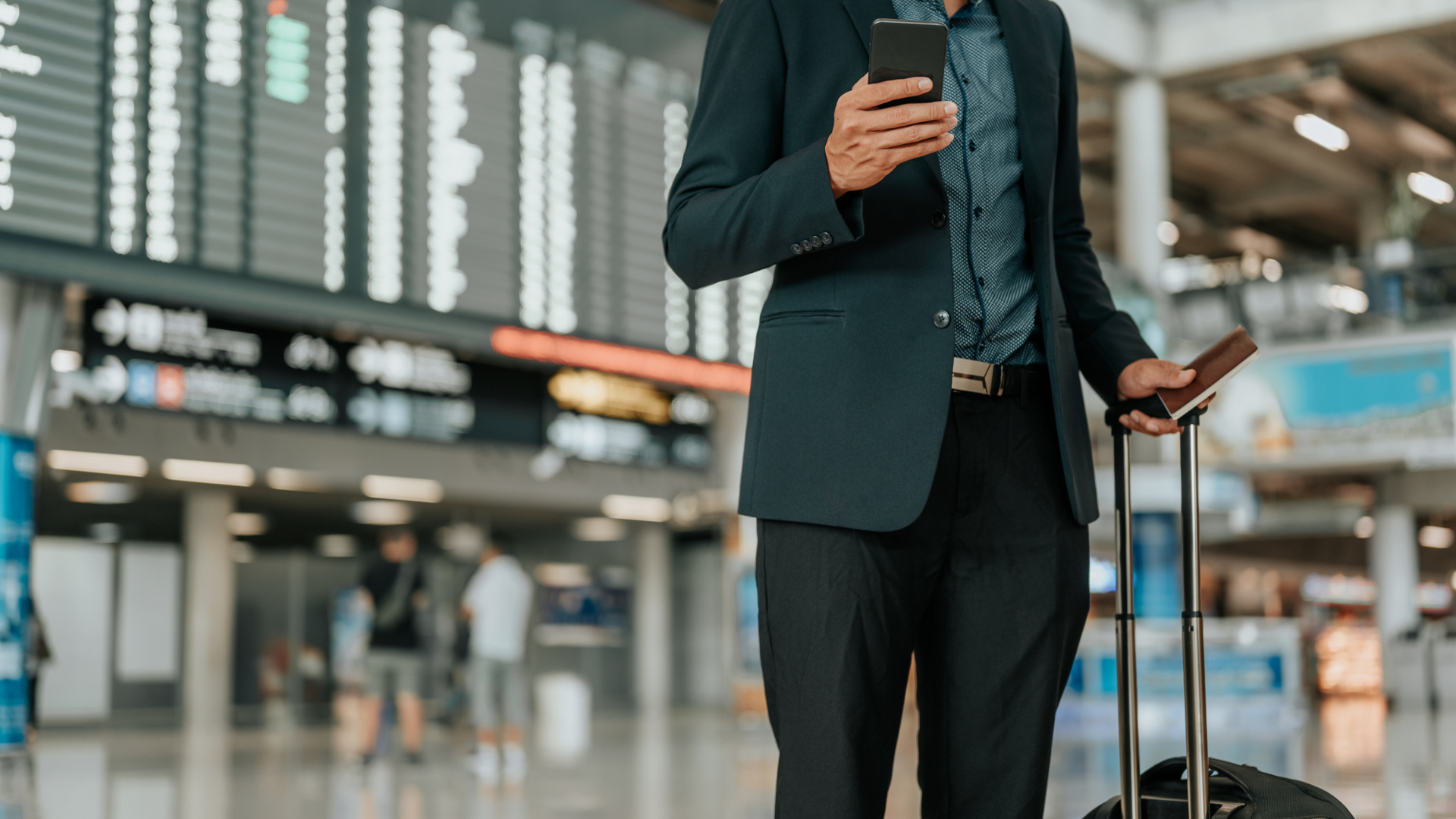 Businessman at the airport, holding a suitcase in one hand and a phone in the other.