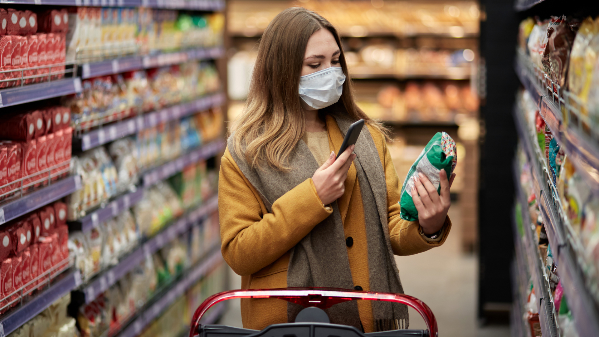 A woman wearing a face mask while shopping in a grocery store, surrounded by shelves of products.