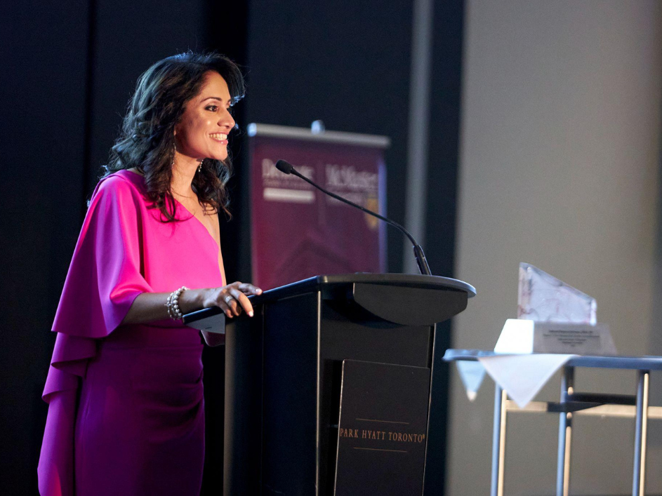 Indrani Butany, dressed in a pink gown, addresses the audience during her speech.