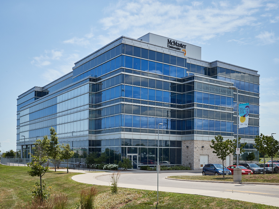 A wide shot of the McMaster Ron Joyce Centre, showcasing its large glass facade under bright daylight.