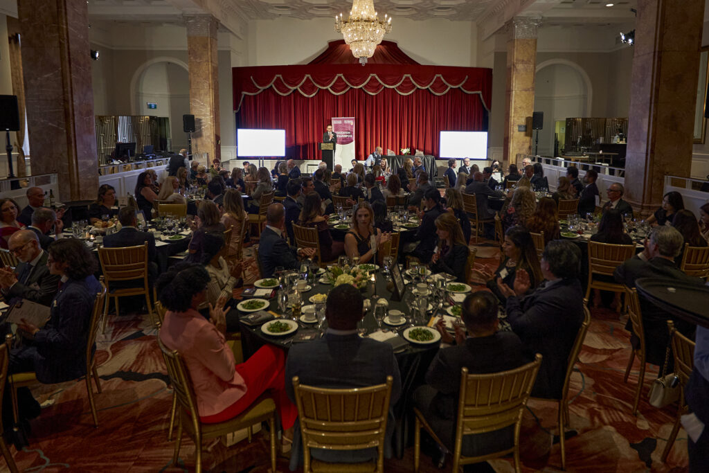 A large group of guests seated at tables in a spacious dining hall, engaged in conversation during dinner.