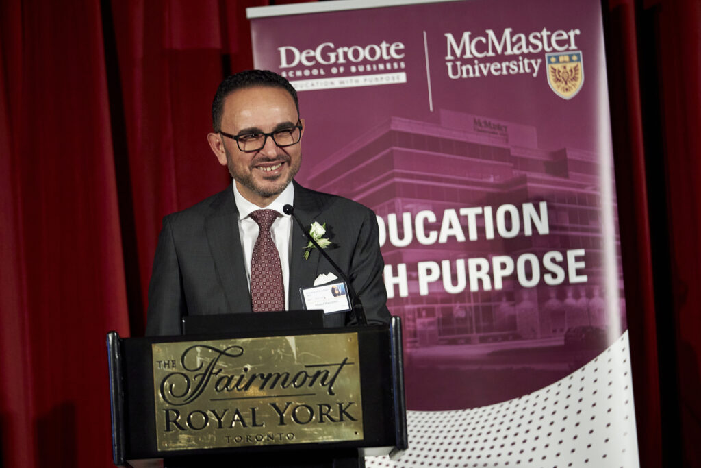 Dr. Khaled Kassanein, wearing glasses and a suit, speaks at a podium during the Accolades dinner event.