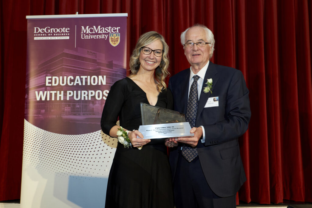 Claire Gillies and Wayne C. Fox stand beside a podium, proudly holding an award together in a celebratory moment.