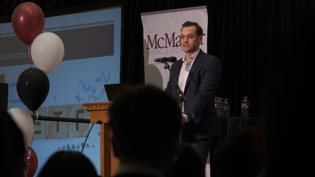 A man in a suit, Blake Cluff, stands confidently at a podium, delivering a presentation.