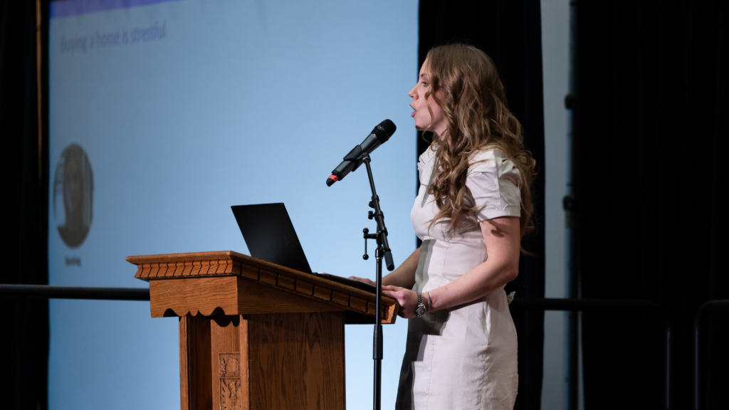 Side profile of Caitlin Bryant presenting at a podium with a laptop.