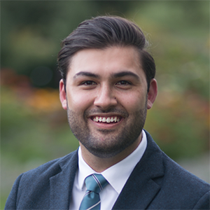 Adam Eqbal smiling confidently while dressed in a formal suit and tie.