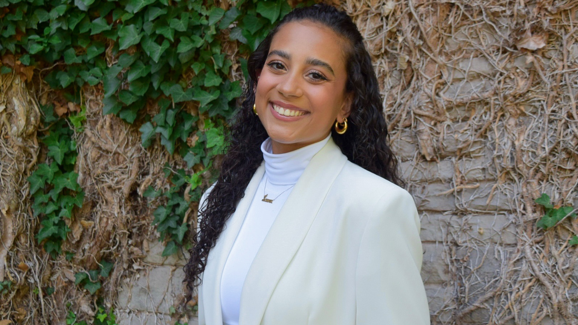 Laura Coelho smiles while wearing a white blazer and white shirt, embodying a stylish and professional appearance.