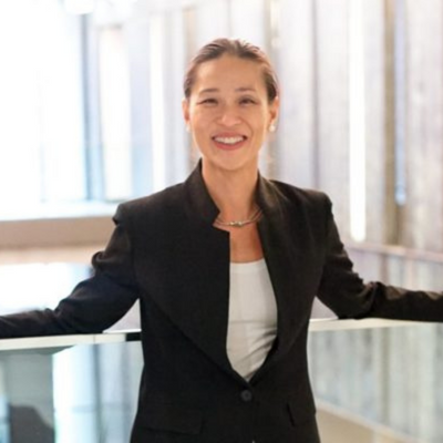 Candice Chow, dressed in a business suit, stands near a railing with a smile.