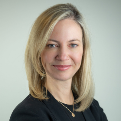 Claire Gillies, a woman with blonde hair, smiles while dressed in a stylish black blazer.