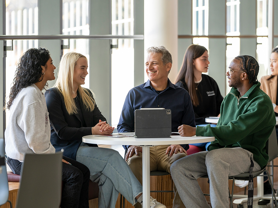 Three DeGroote students and a professor engaged in a lively discussion around a table in a collaborative setting.