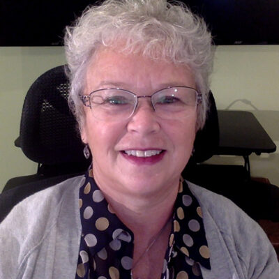 Frances Tuer, wearing glasses and a polka dot shirt, smiles while seated in her office chair.