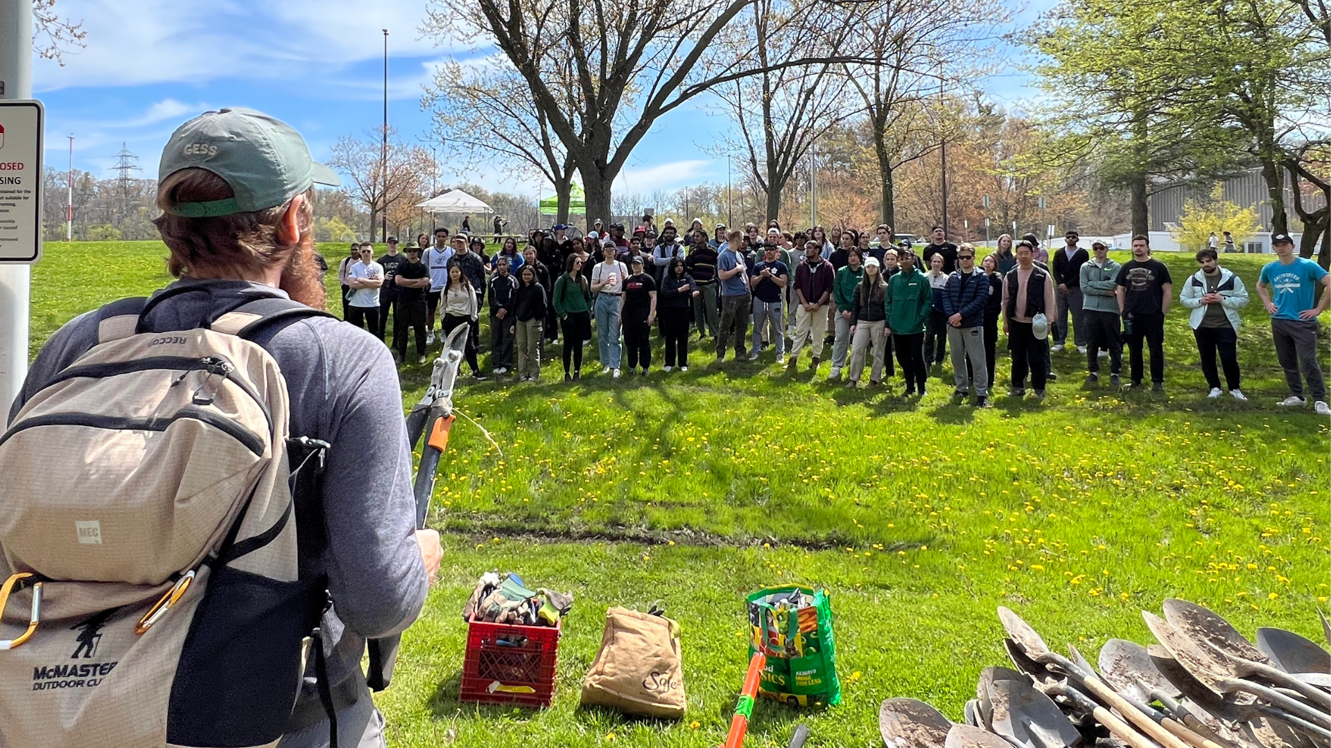 Greensuits commerce students gather in a park with backpacks, ready to launch their sustainability initiative.