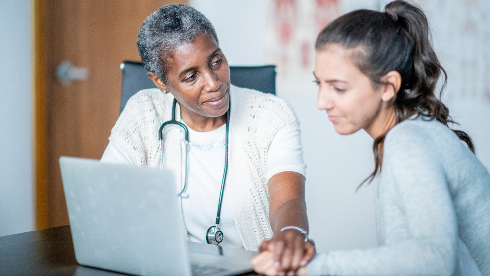 A woman and a doctor converse while looking at a laptop.