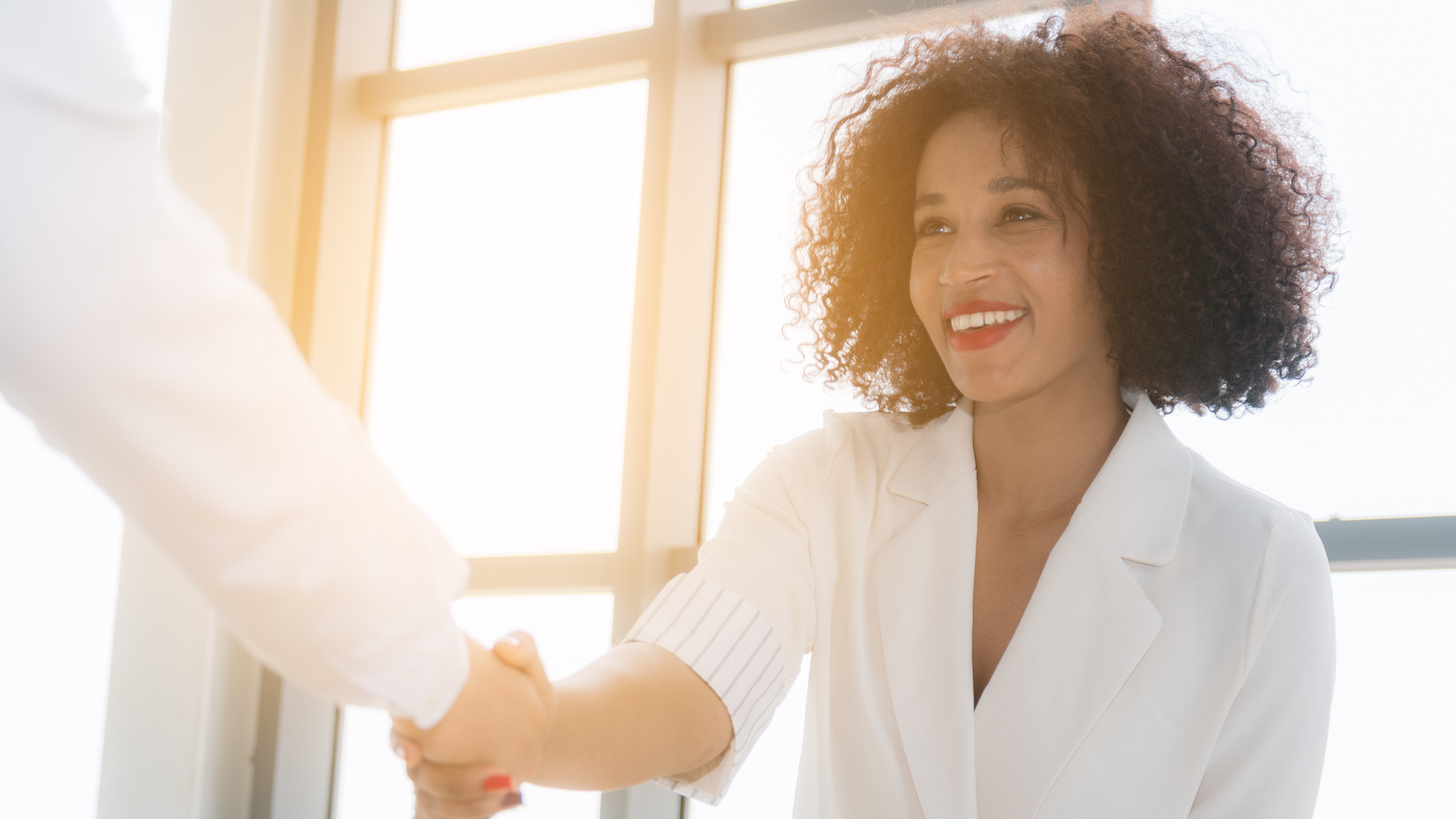 A woman shakes hands with another woman, symbolizing collaboration and connection in the workplace.