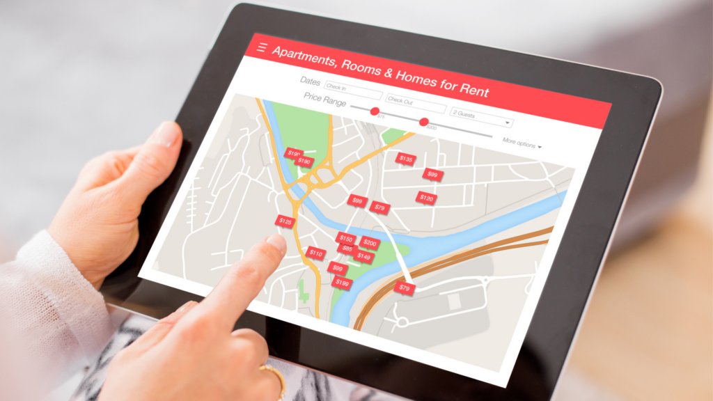 Close-up of hands holding a tablet displaying a city map with listings for apartments and homes available for rent.