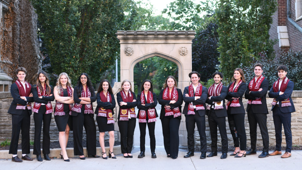 DeGroote JDCC team in black suits and maroon scarves smiles in front of McMaster Edwards Arch.