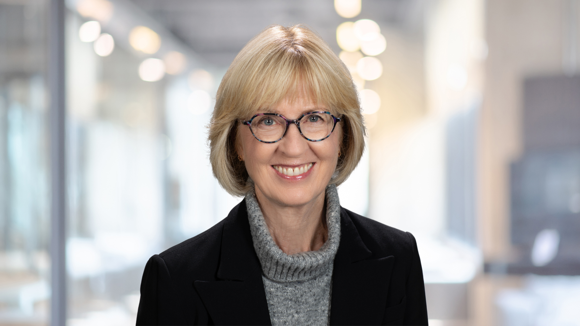 Jane Peverett, smiling brightly and wearing a grey sweater and black jacket.