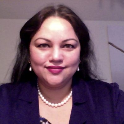 Lobana Jodie, a woman with long black hair, smiles while wearing a pearl necklace.