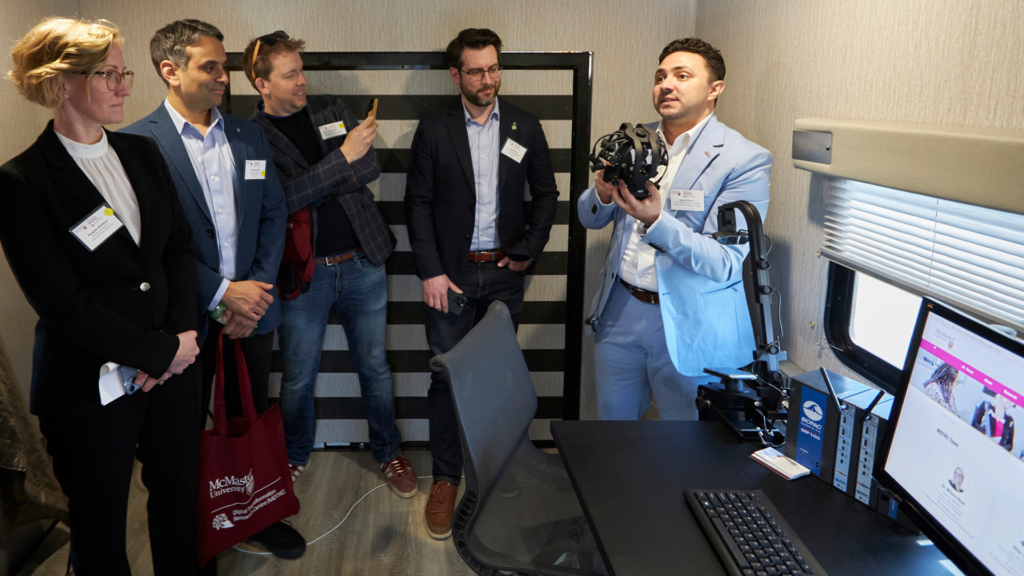 A group of individuals gathers around a computer, while Nour El Shamy displays a brain wave device in the mobile lab.